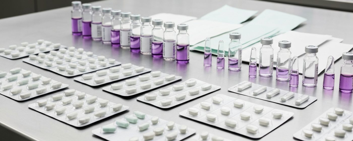 Pharmaceutical blister packs and glass vials on a stainless steel surface in a sterile filling facility